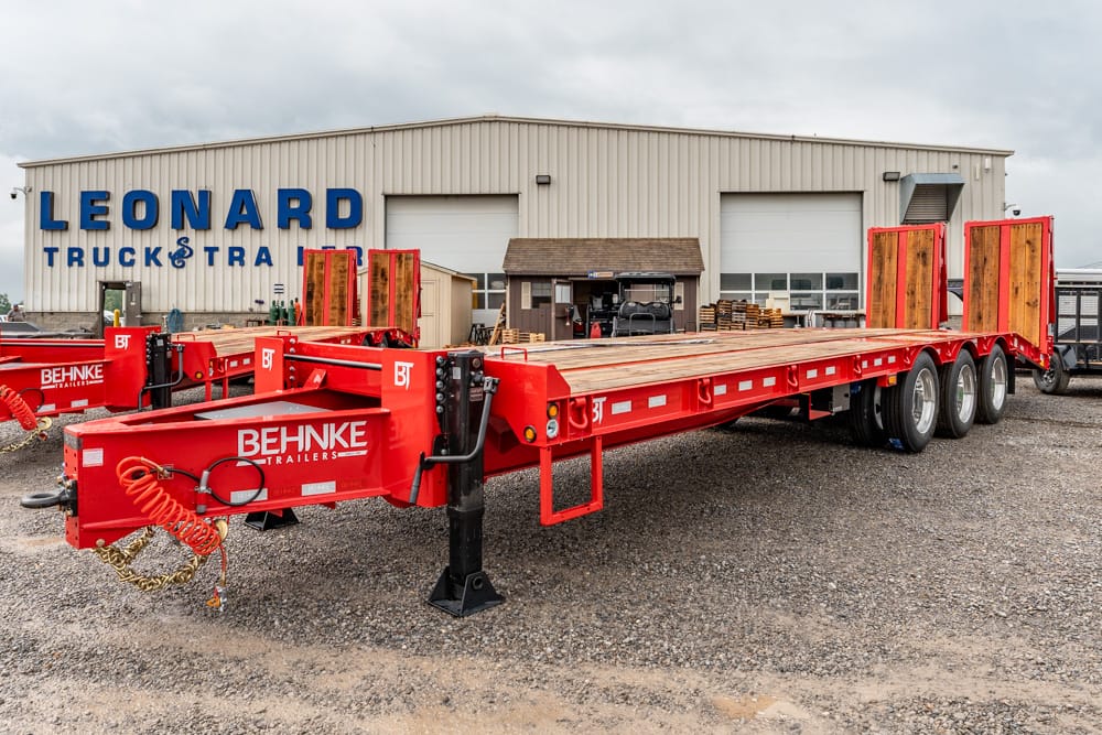 Red Behnke trailer with long flatbed parked in front of an industrial building marked Leonard Truck & Trailer.