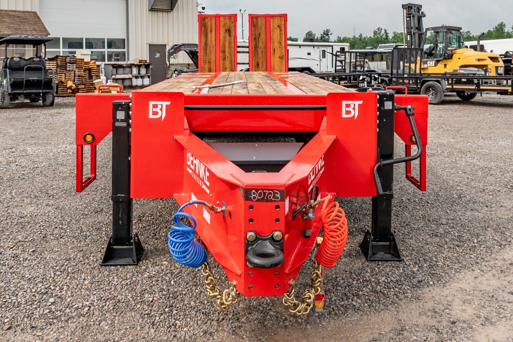 Red BT heavy trailer with wood deck and stabilizing legs, parked on a gravel lot in an equipment yard.