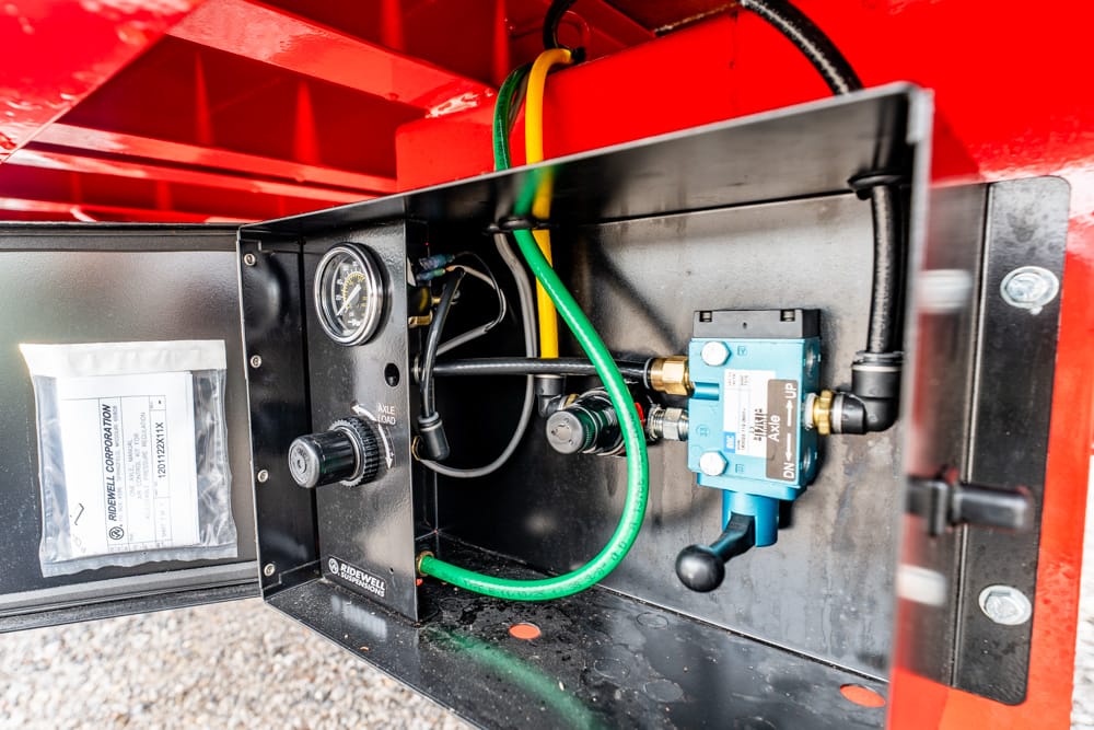 Open access panel with a round pressure gauge, black knob, and green hose connected to a blue solenoid valve inside a red enclosure.