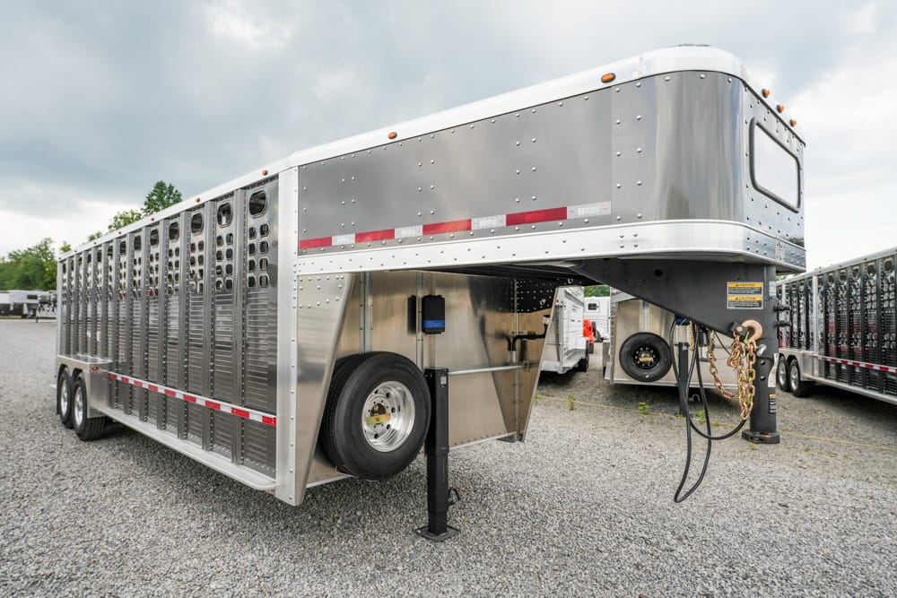 Silver gooseneck livestock trailer parked on gravel, with ventilation vents along the side.