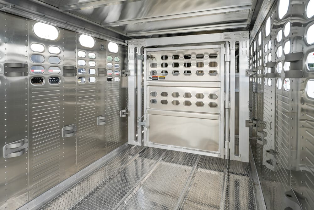 Interior of an aluminum livestock trailer with ventilated side walls and a rear gate/door at the far end.