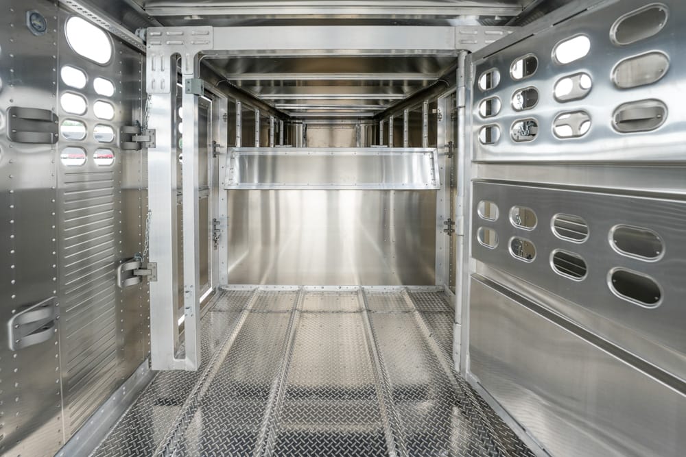 Inside a gleaming empty metal transport trailer with a diamond-plate floor and a partition at the far end.