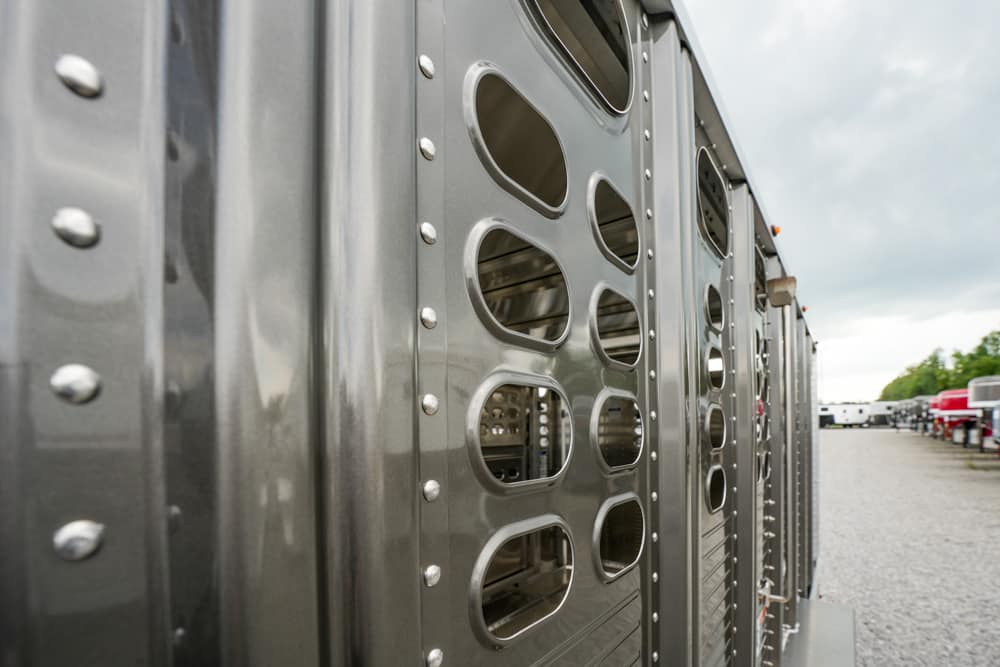Row of gray metal trailers with oval vent openings and riveted panels lined up side by side in a lot.