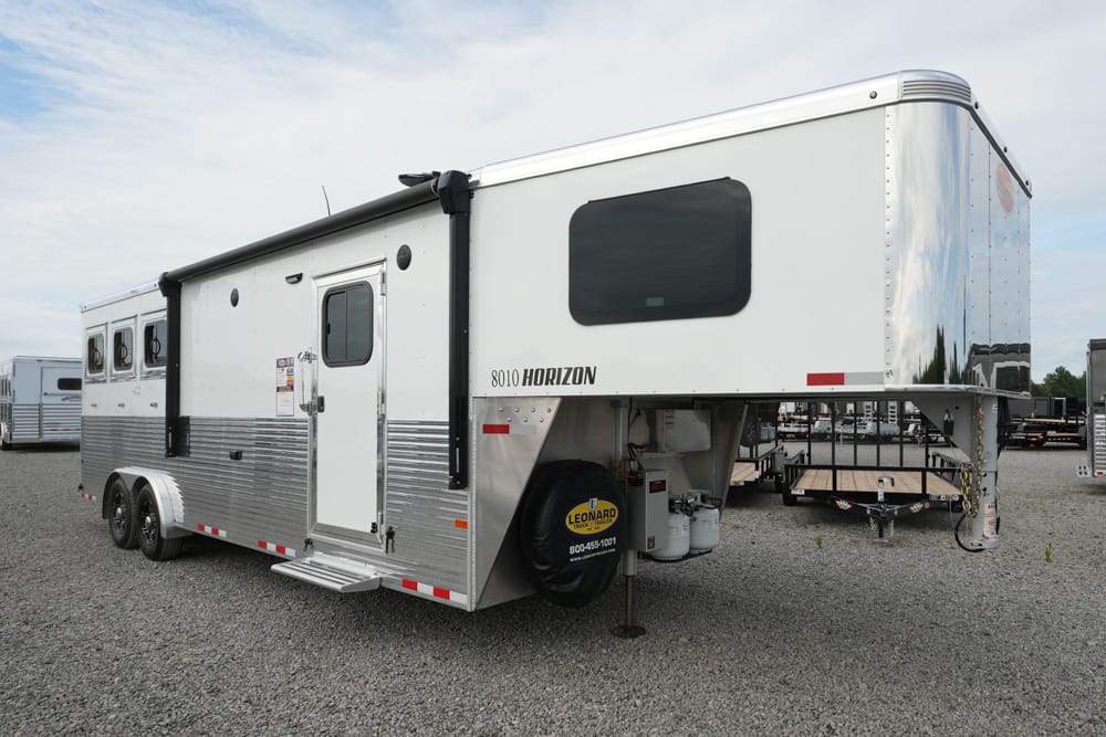 White Horizon 8010 gooseneck trailer with two axles, side entry door, and raised living quarters on a gravel lot.