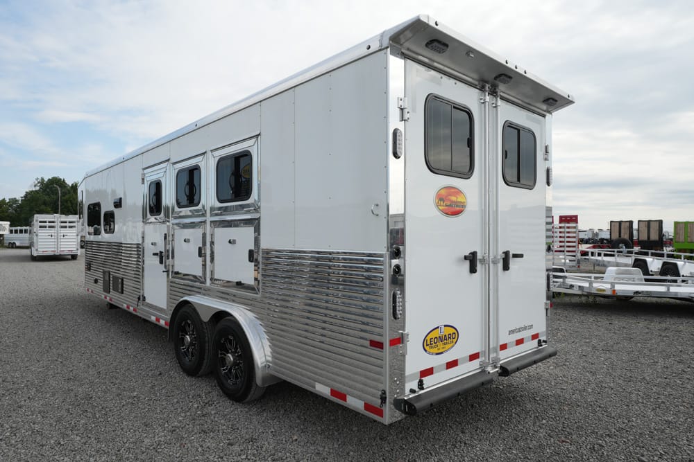White horse trailer with two rear doors, windows, and chrome ribbed lower siding parked on gravel lot