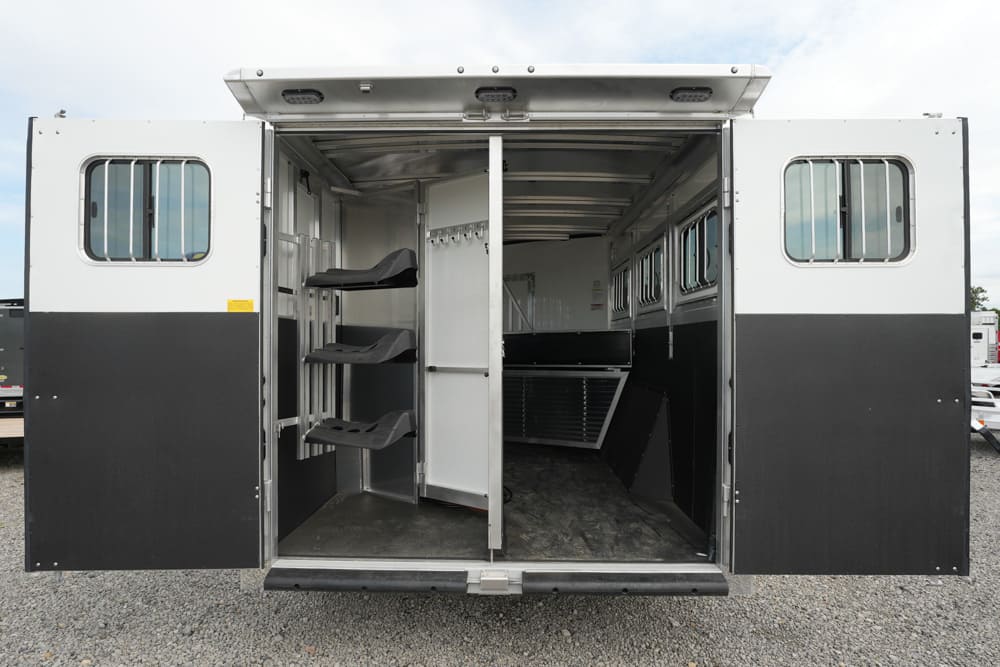 Open horse trailer interior with a partition, saddle racks on the left, and windows along the right wall.