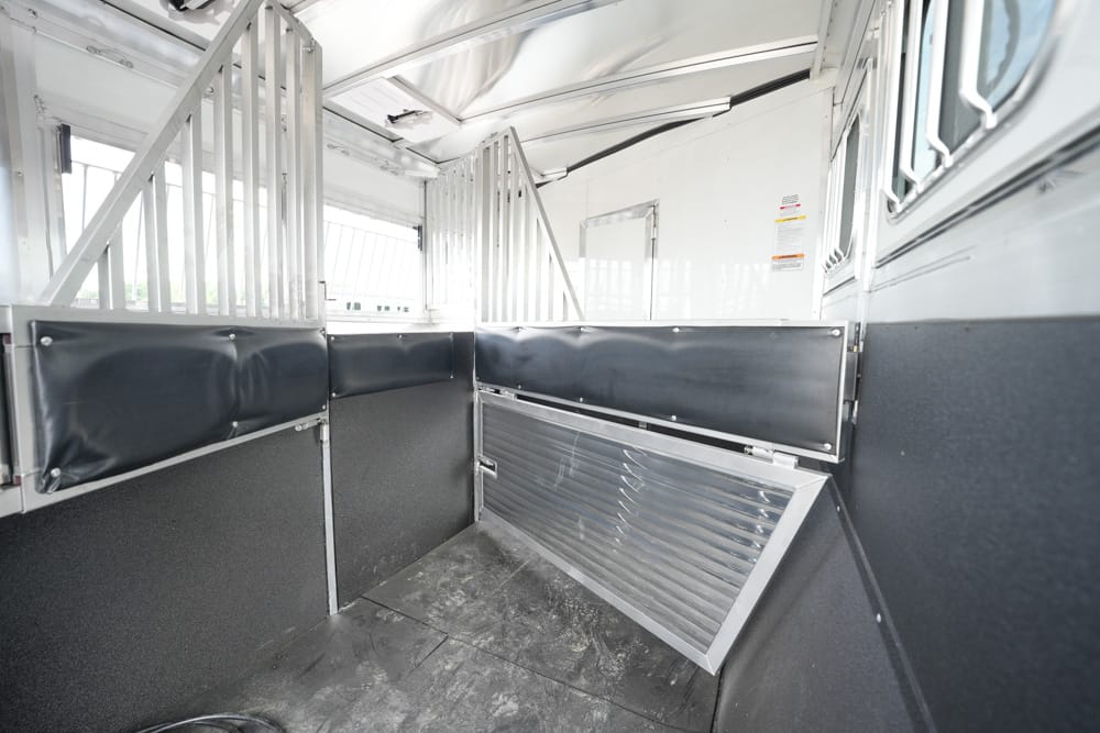 Inside of a horse trailer with partition stalls, padded black walls, and a raised metal ramp at the back.