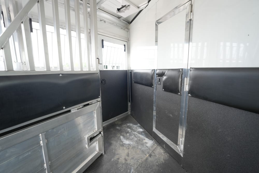 Interior of a metal horse trailer with black padded walls and a partitioned stall area, metal floor and divider doors visible.