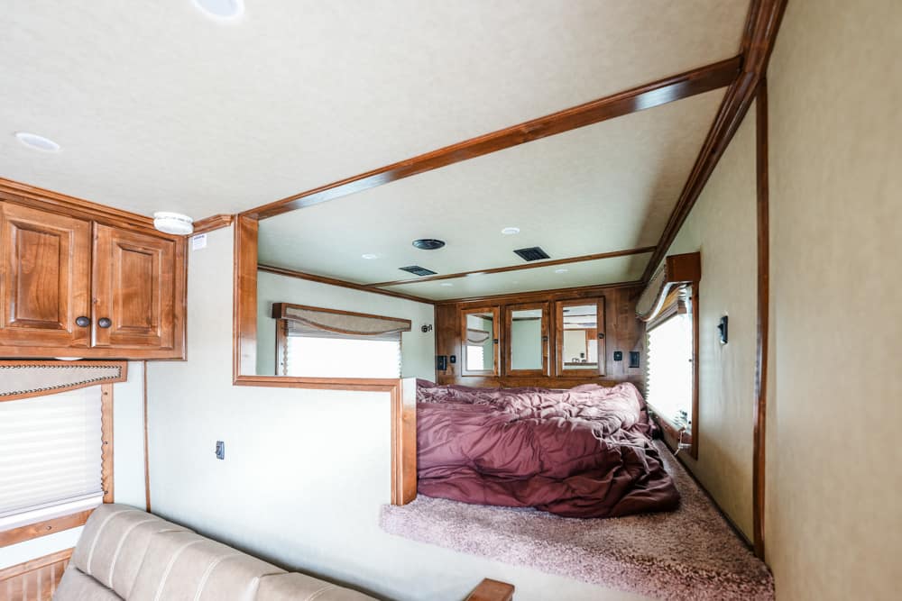 Interior of a cozy RV bedroom with wood cabinets, a large bed with burgundy bedding, and beige walls.