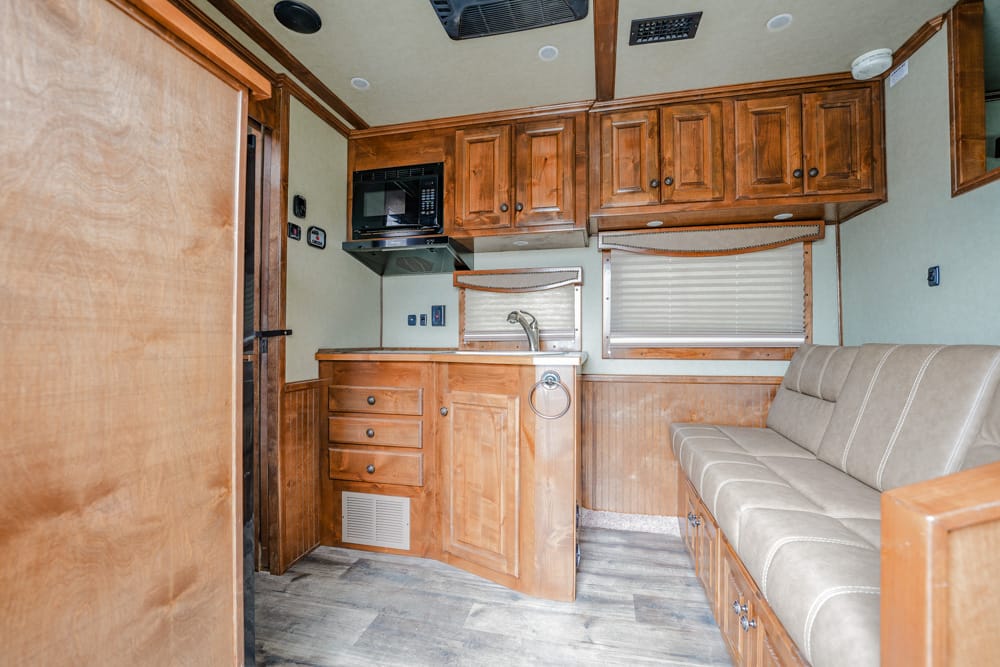 Wood-paneled RV kitchen with cabinets, sink, microwave, and beige sofa along the wall