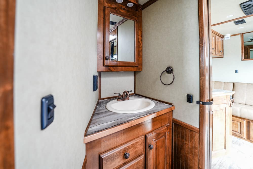 Wooden RV bathroom vanity with marble countertop, sink, and wall mirror in a compact space.