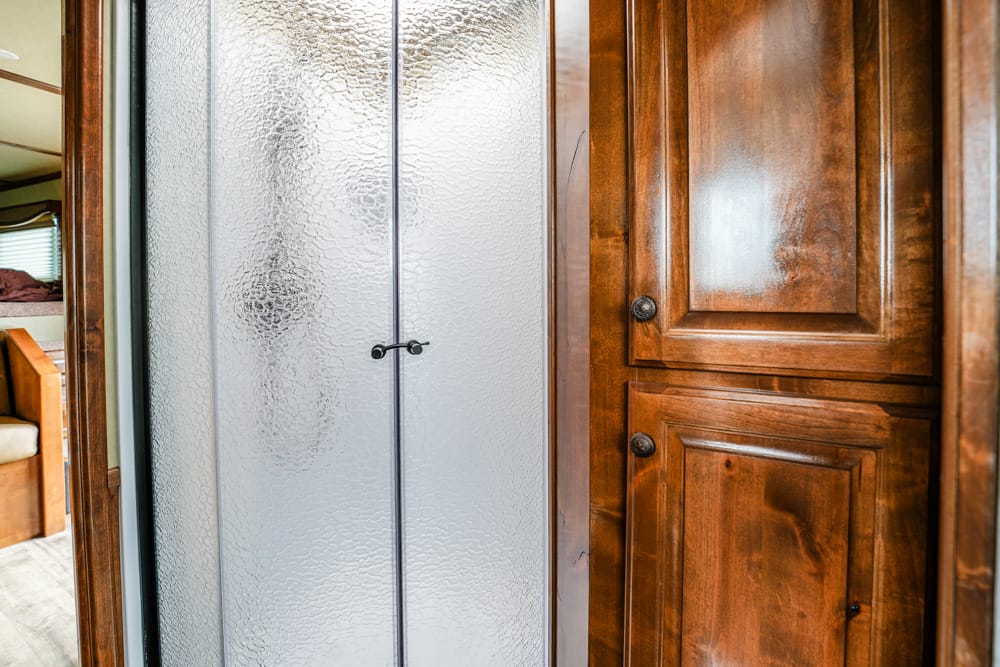 Frosted glass shower doors with small black handles, beside polished dark wood cabinets in a compact bathroom setting.