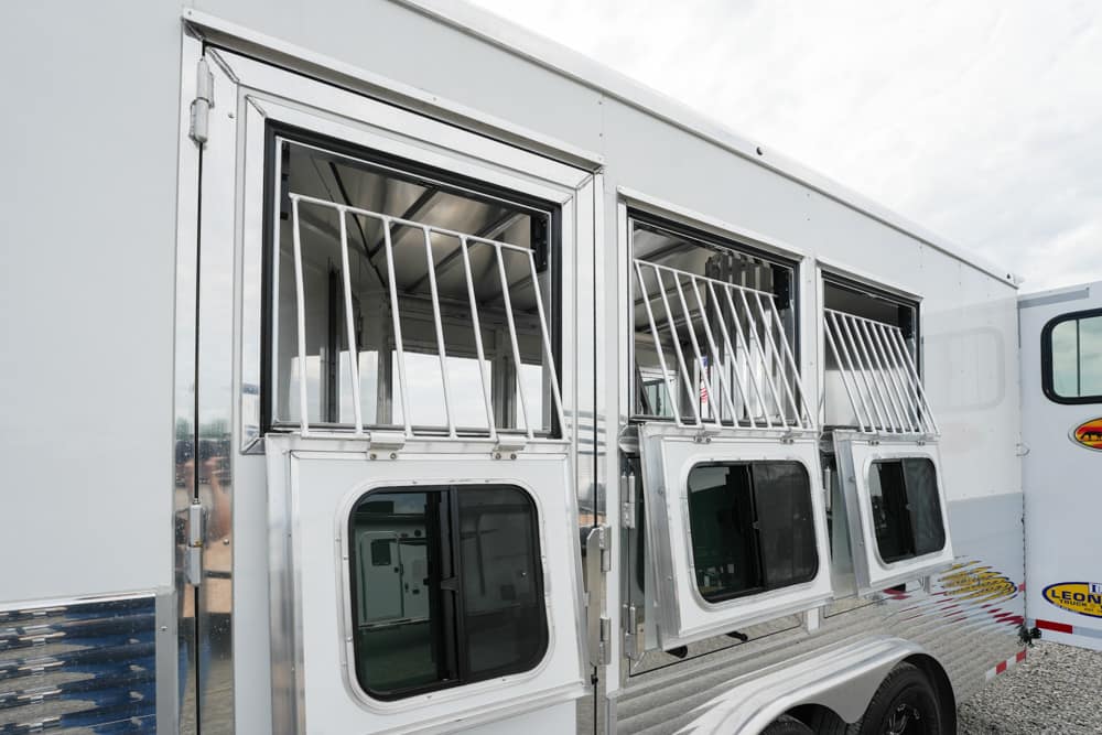 Silver horse trailer with three ventilated, barred stall windows along the side.