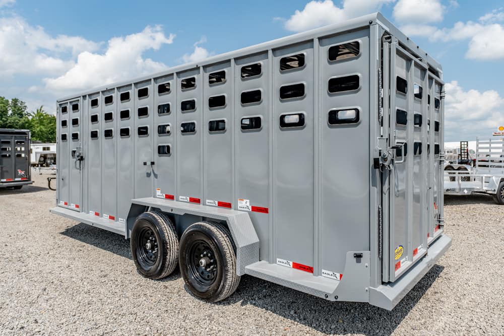 Gray livestock trailer with multiple ventilation windows parked on a gravel lot, two-axle design with black wheels.