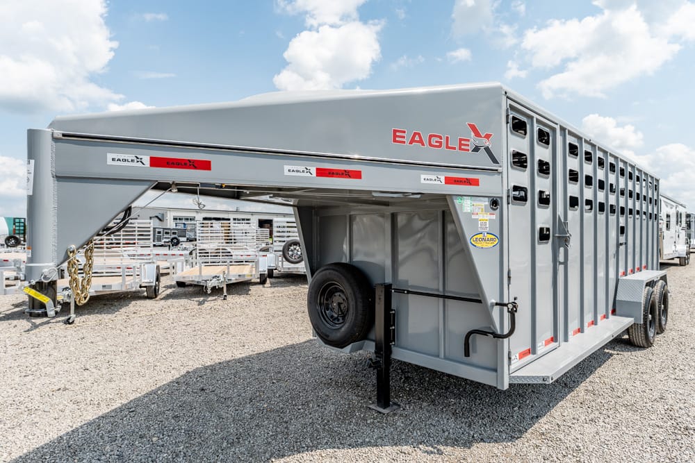Gray Eagle gooseneck livestock trailer on a gravel lot, with spare tire, ventilation windows, and red reflective strips.