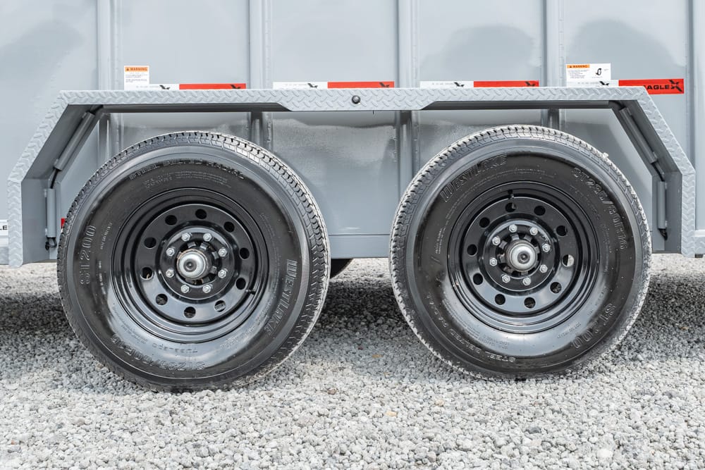 Dual black steel wheels on a gray utility trailer, resting on gravel.