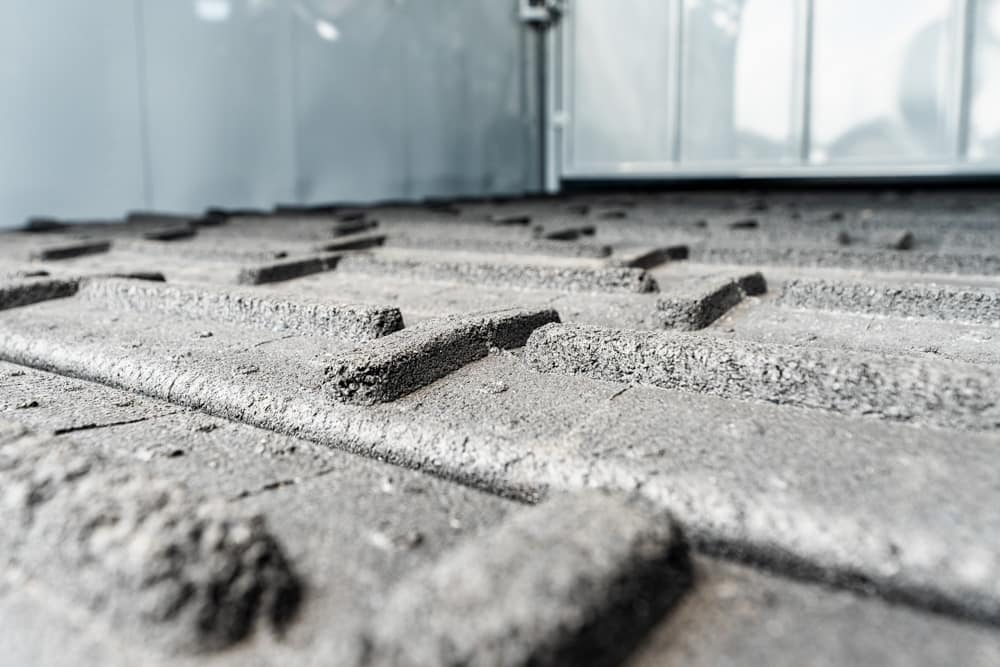 Close-up of textured concrete pavers arranged in a grid, with a glass building in the background.