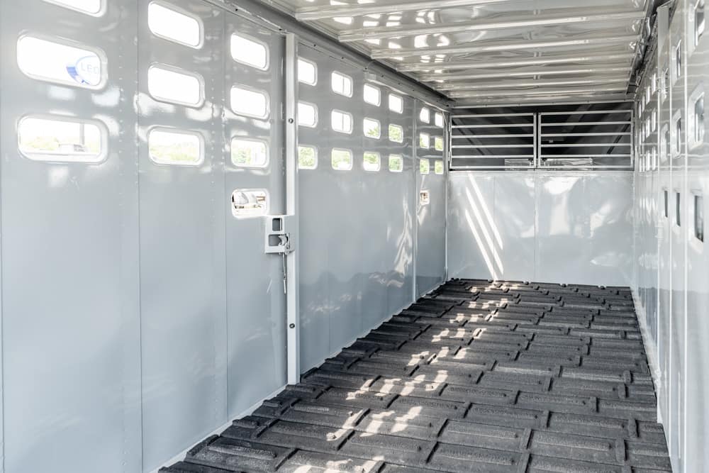 Empty gray livestock trailer interior with side windows and ribbed rubber floor ready for loading.