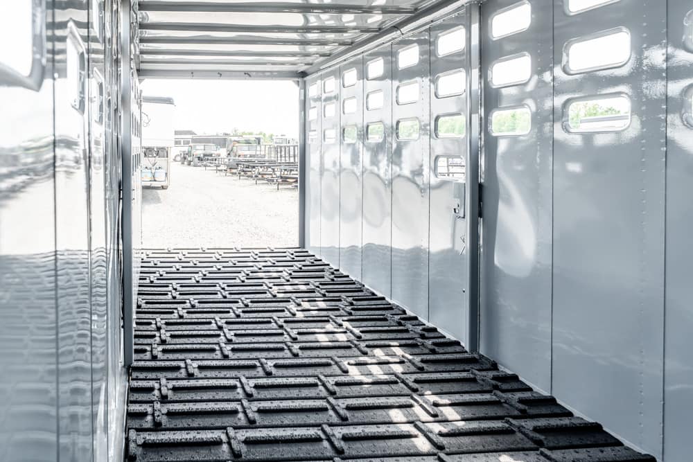 Interior view of a shiny metal trailer with ribbed floor, looking toward an open rear doorway to a yard with equipment outside