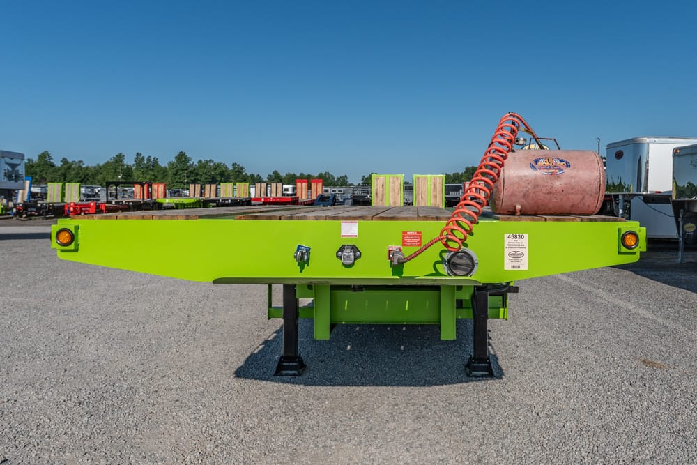 Bright green flatbed trailer in a truck yard with an orange coiled hose and pink tank on top.
