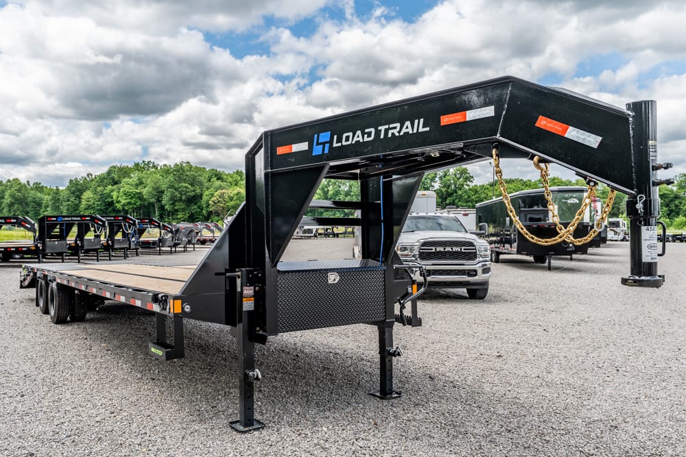 Black Load Trail gooseneck trailer on a gravel lot, with safety chains and a toolbox in the neck area.