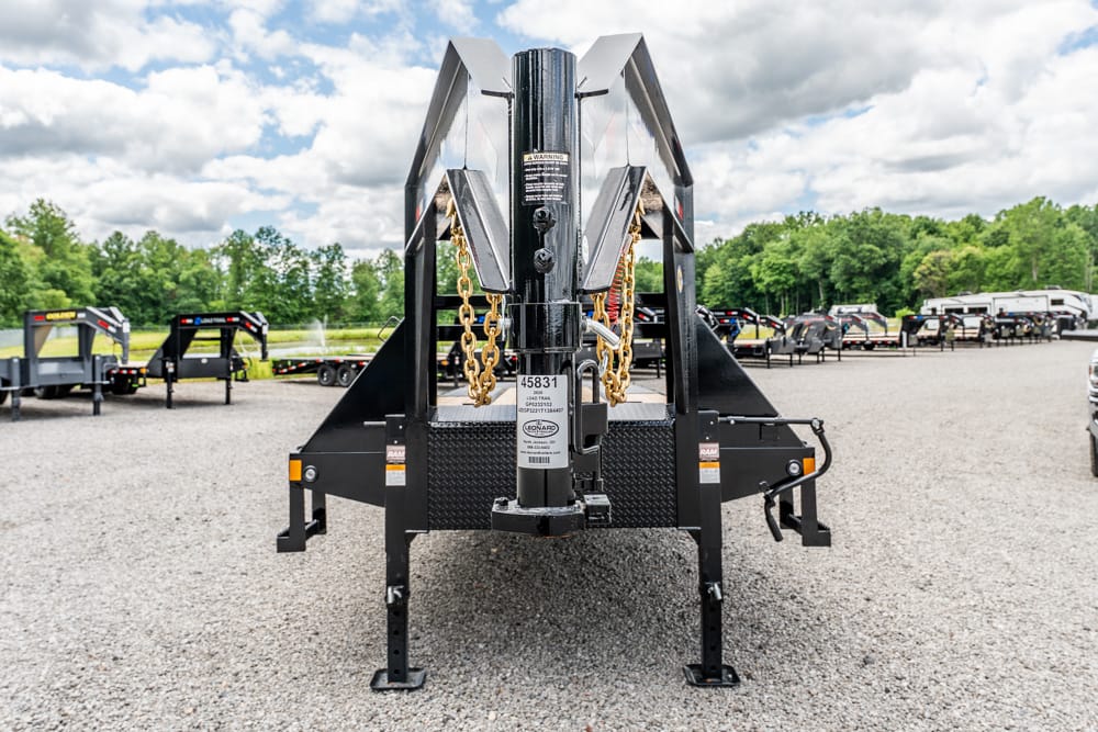 Front view of a black heavy-duty trailer hitch with safety chains, parked on a gravel lot.