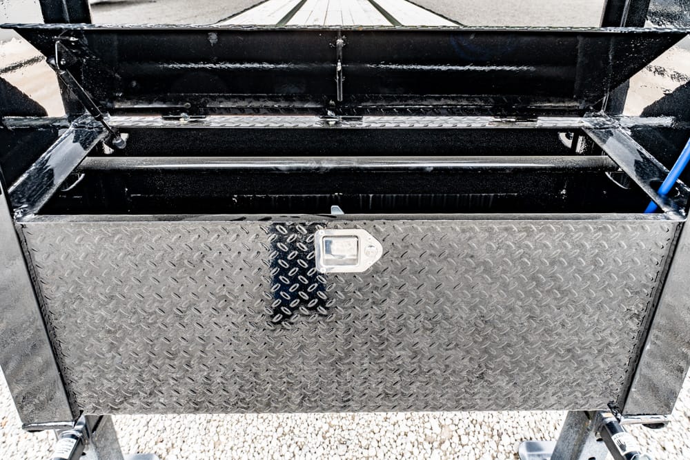 Open diamond-plate utility toolbox on a trailer with a latch and metal frame storage area above.