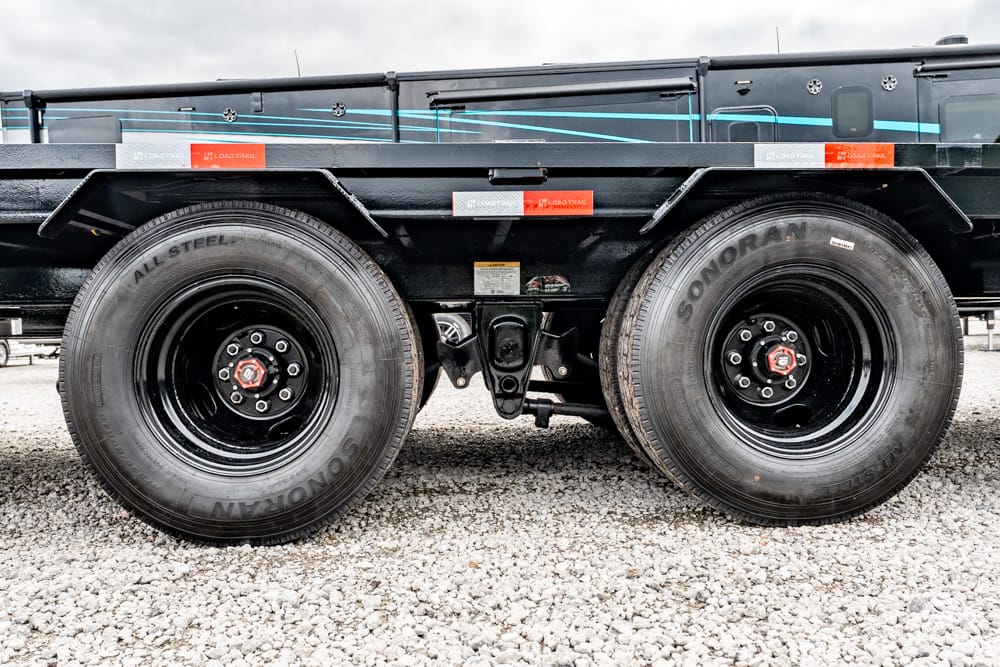 Close-up of dual trailer wheels with black rims on a gravel surface