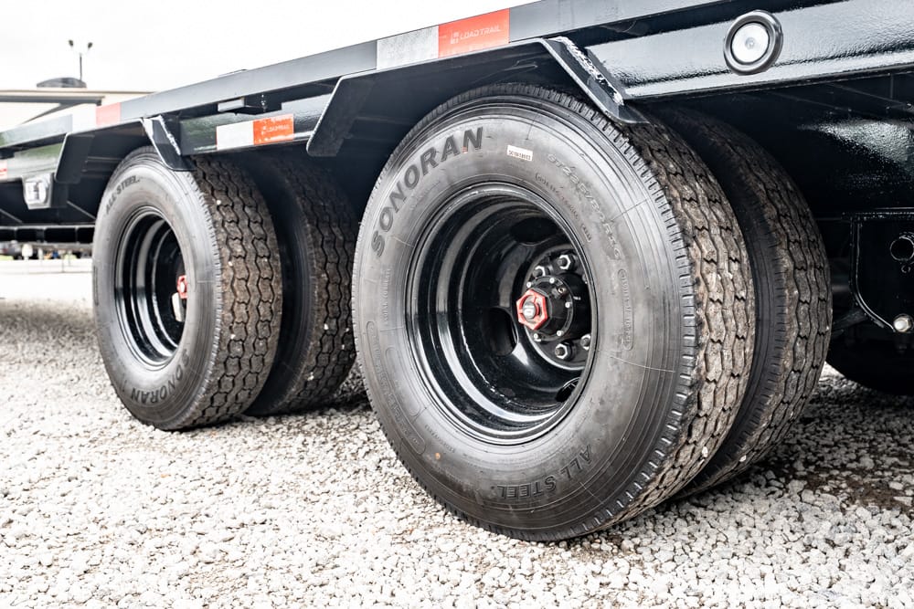 Close-up of three trailer wheels in a row on a gravel surface, showing black rims and treaded tires on a heavy-duty trailer.