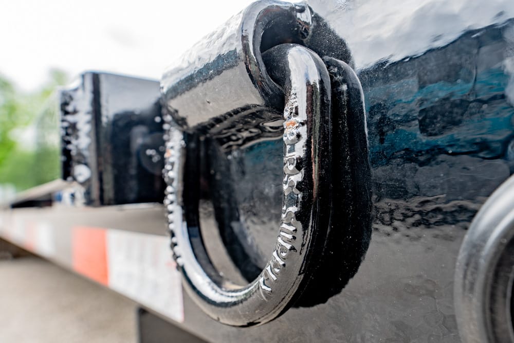 Close-up of a heavy metal padlock securing a trailer hitch on a black trailer with red‑white reflective stripes.