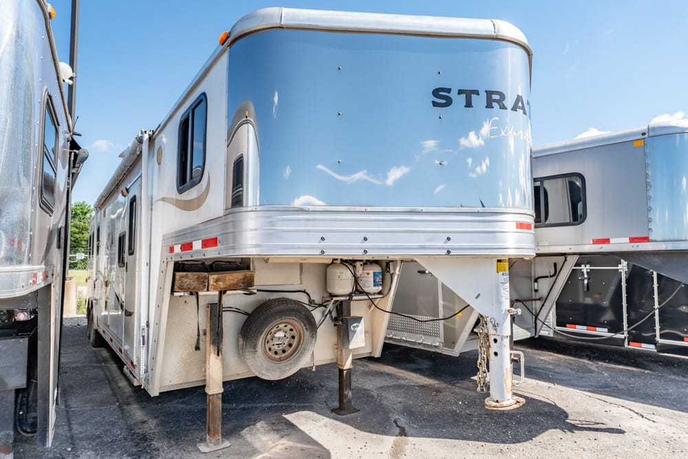 A large, blue and white fifth-wheel trailer parked in a lot with its landing gear down and spare tire visible undercarriage