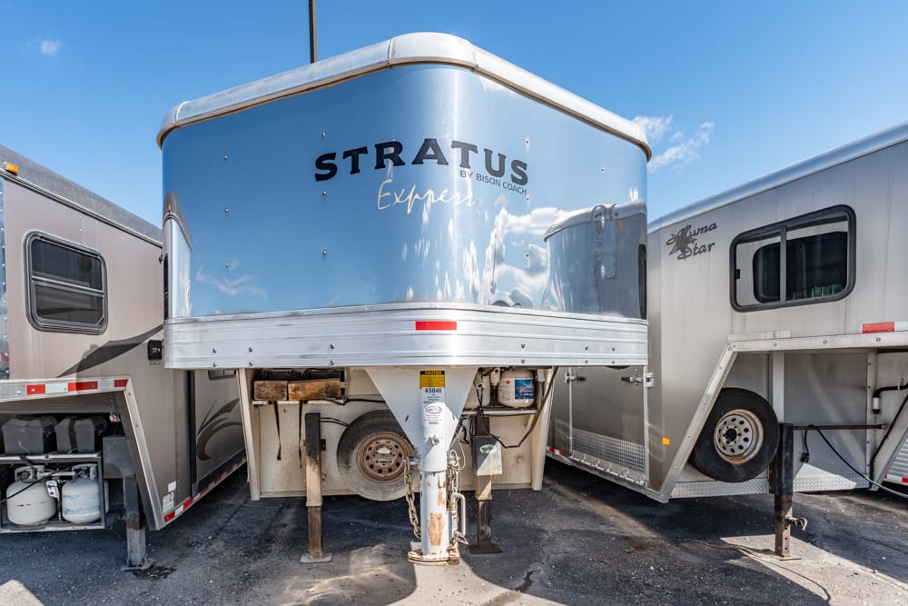 Front view of a blue Stratus Express trailer with chrome trim parked between two silver trailers on a sunny day, a clear blue sky above.