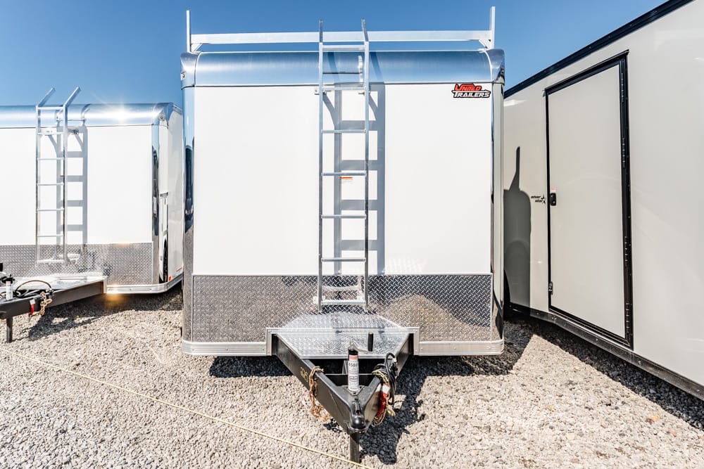 Front view of a white enclosed trailer with a diamond-plate skirt and a metal ladder on the nose area near the hitch.