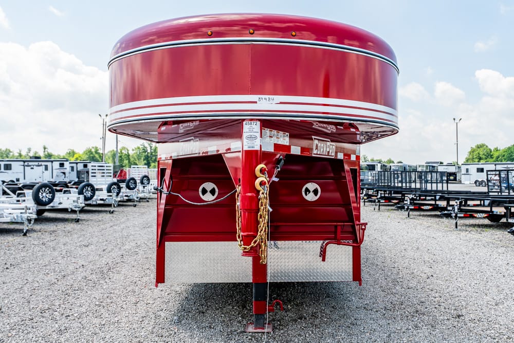 Red gooseneck trailer with a rounded tank, parked in a gravel trailer yard.