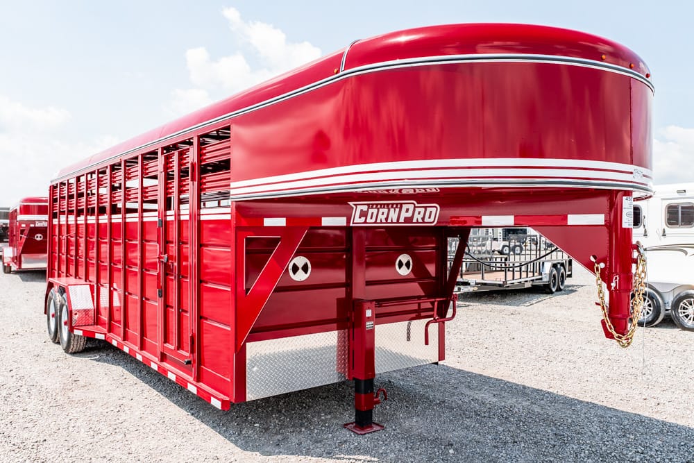 Red gooseneck livestock trailer parked on a gravel lot, with CORN PRO branding visible on the side panel.