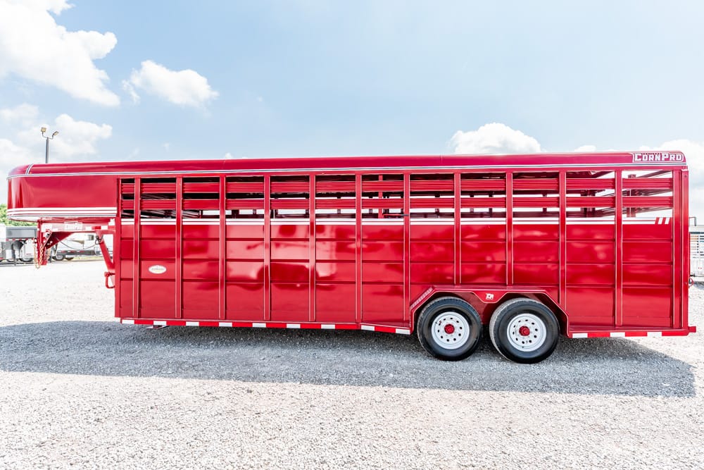 Long red livestock trailer with vented sides parked on a gravel lot under a blue sky