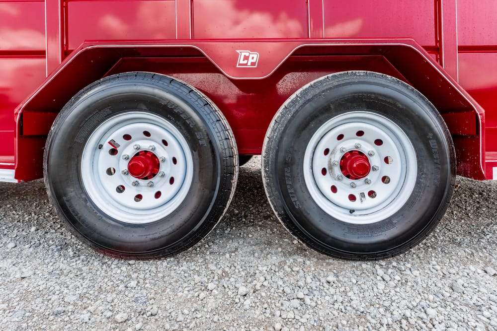 Dual wheels on a red trailer with silver rims and red center caps on a gravel surface.