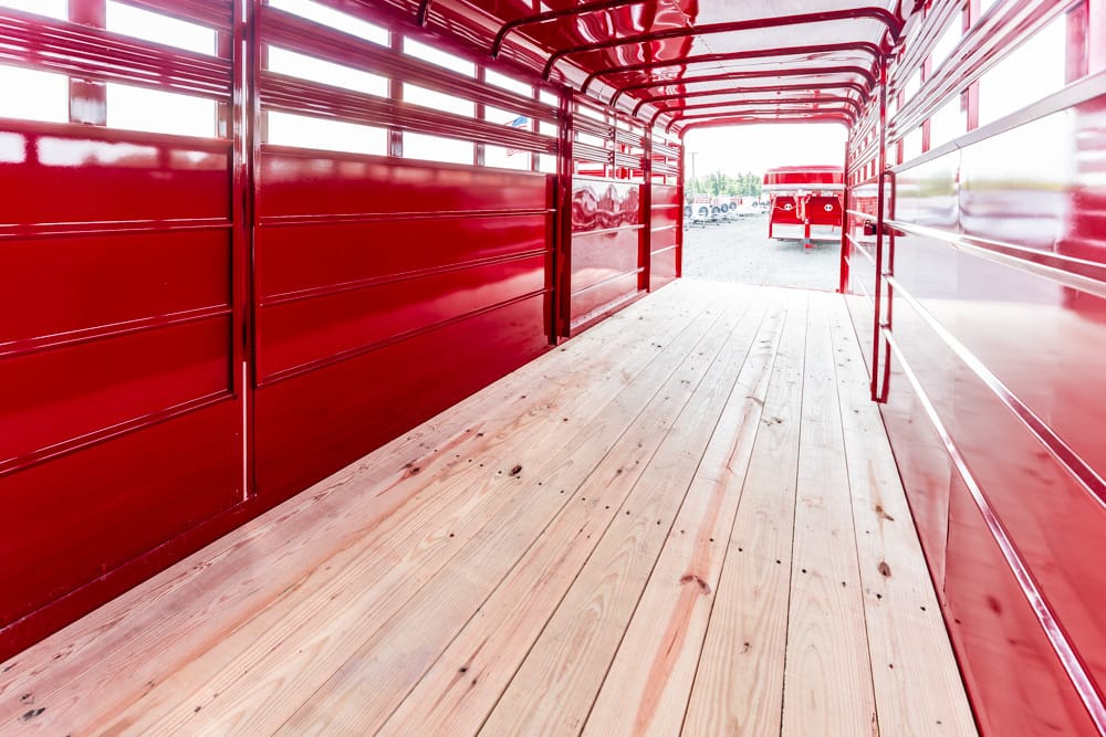 Interior of a red cargo trailer with wooden planks, viewed from inside toward the open back where another trailer is visible outside
