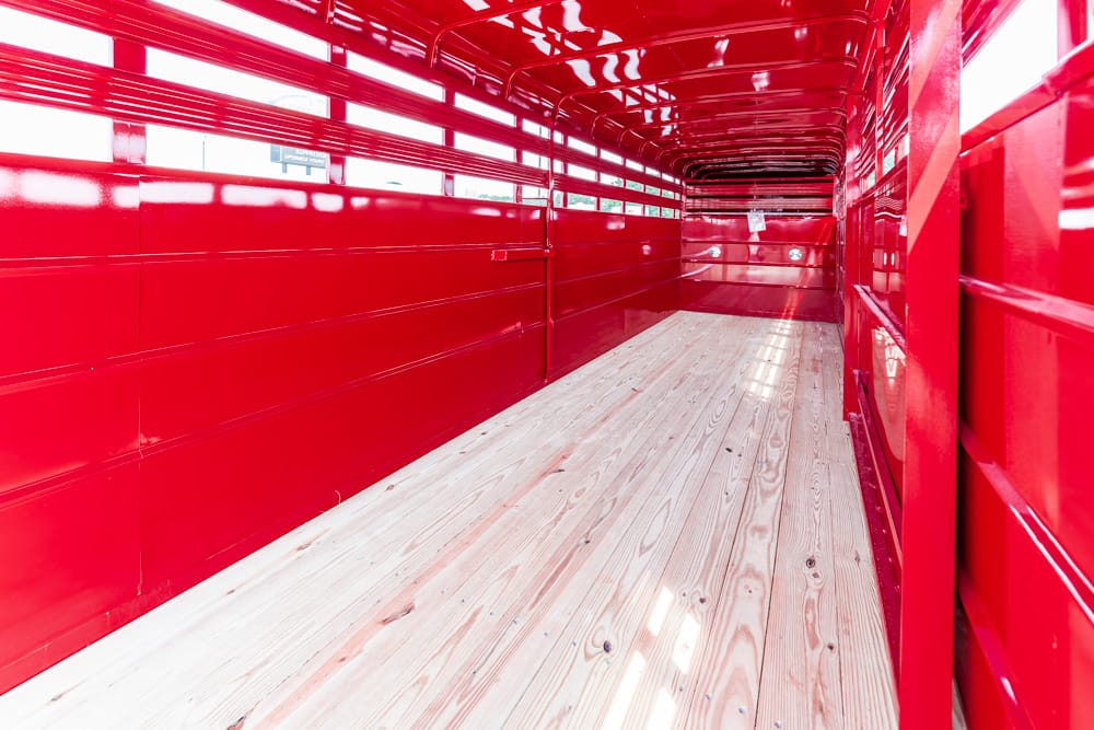 Interior of a bright red cargo trailer with glossy metal walls and a wooden plank floor, empty and well-lit.