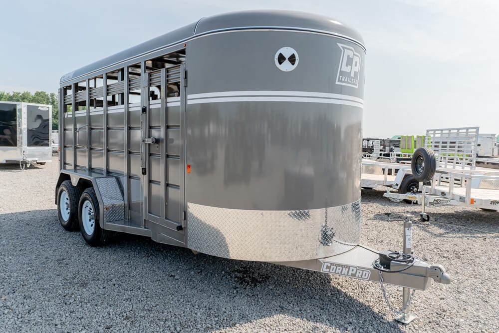 Gray bumper-pull livestock trailer with three side doors and diamond-plate front on a gravel lot.