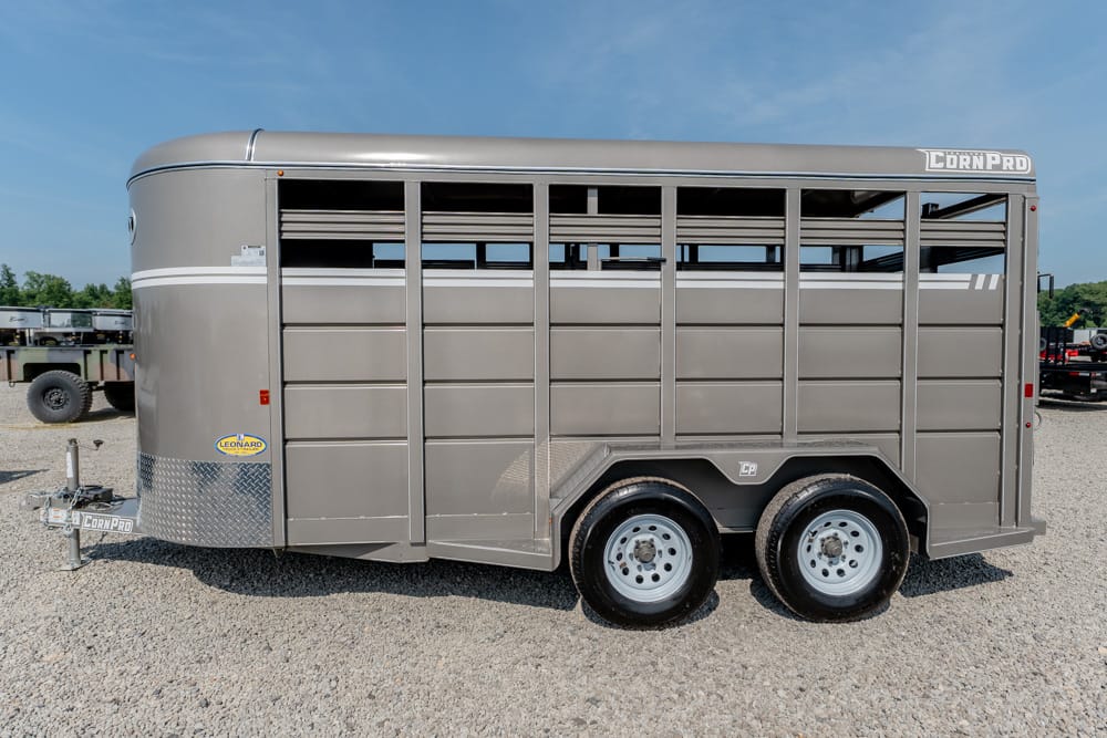 Gray CornPro livestock trailer with dual axles parked on gravel, vents along the top, and diamond-plate front section.