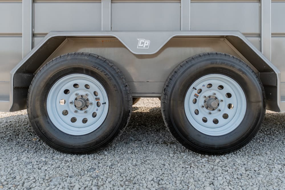 Dual trailer wheels and fender on a gray metal trailer, parked on gravel.