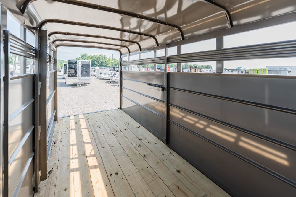 Interior of a metal trailer with a wooden floor, open rear gate, and other trailers visible in a lot outside.