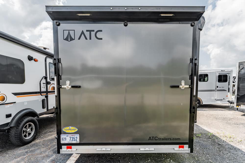 Rear view of a silver ATC trailer with closed doors, showing the ATC logo and website atctrailers.com, in a lot with other RVs nearby.