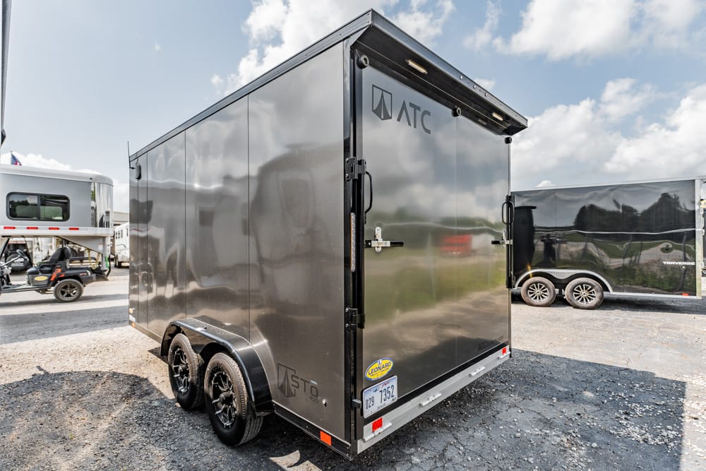 Gray enclosed cargo trailer with dual rear doors and ATC logo, parked on gravel, others trailers visible in background