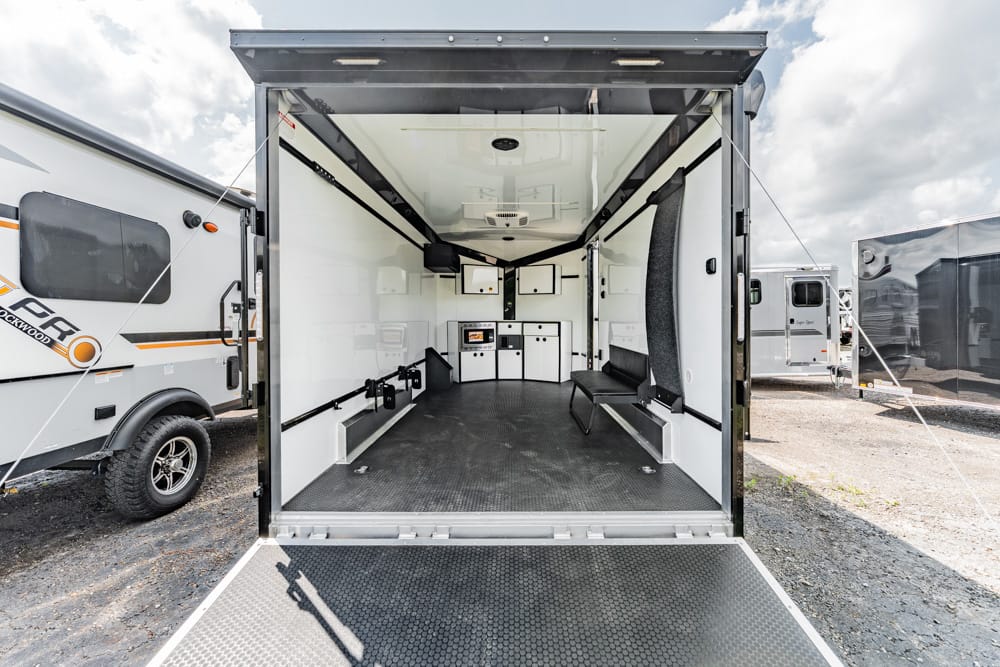 Open mobile trailer interior with white cabinetry, bench seating, and a black rubber floor, ready for equipment use