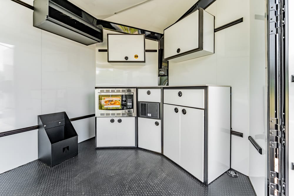 Mobile kitchen interior with white cabinets, a built-in oven, microwave, and curved counter area in a trailer.