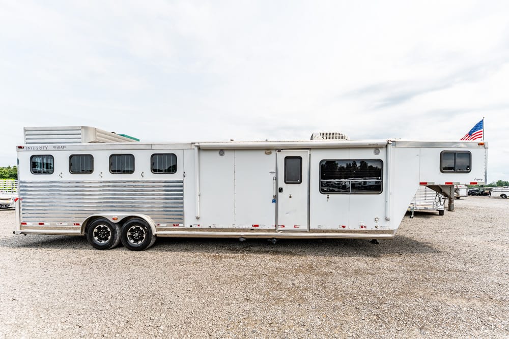 Long silver gooseneck horse trailer with living quarters, parked on a gravel lot with an American flag at the rear