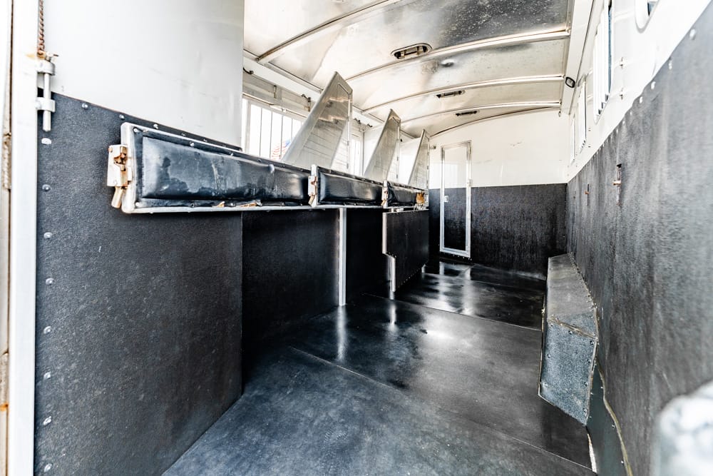 Interior of a mobile food trailer with black counters and metal food bins along the left wall, empty and clean.
