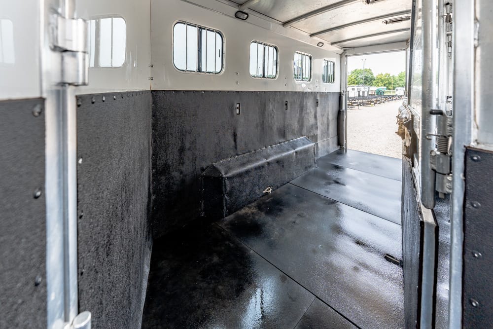 Empty horse trailer interior with black padded walls and small side windows along the top edge, awaiting loading.